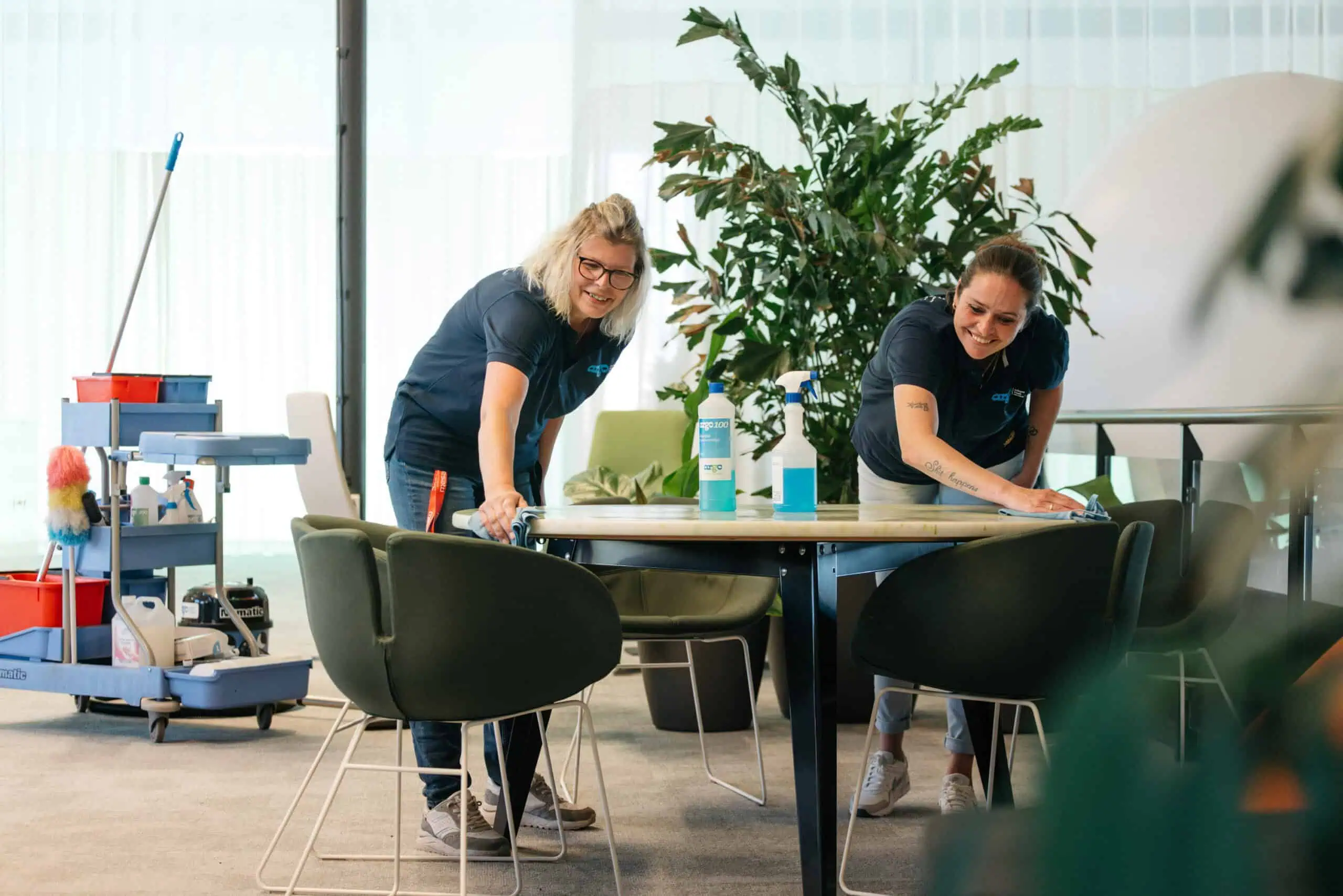 Twee medewerkers van Argo Schoonmaakservice maken een vergadertafel schoon in een kantoorpand